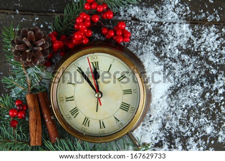 Clock with fir branches and berries on snow on wooden background