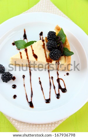 Slice of cheesecake with chocolate sauce and blackberry on plate, on wooden background
