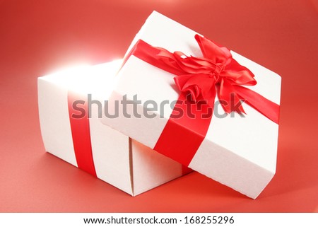 Gift box with bright light on it on red background