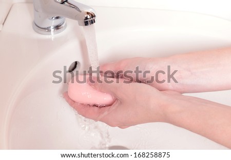 Close-up of human hands being washed under faucet in bathroom