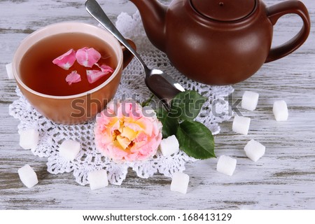 Kettle and cup of tea from tea rose on board on napkin on wooden table