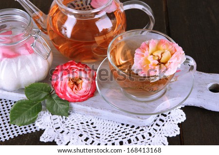 Kettle and cup of tea from tea rose on board on napkin on wooden table