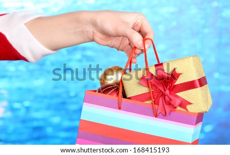 Hand holds package with New Year balls and gifts on blue background