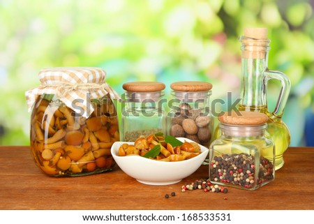 Composition of delicious marinated mushrooms, oil and spices on wooden table on bright background