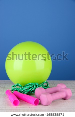 Bright green ball with rope and dumbbells on table on blue background