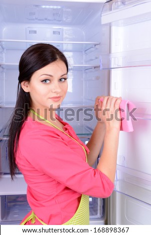 Beautiful young woman washing fridge in kitchen