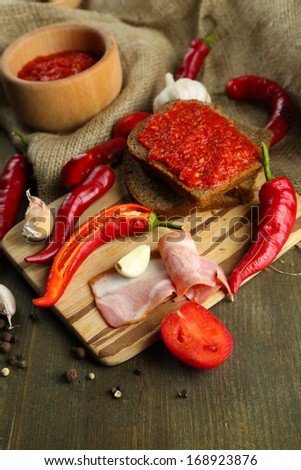 Composition with salsa sauce on bread,, red hot chili peppers  and garlic, on sackcloth,  on wooden background