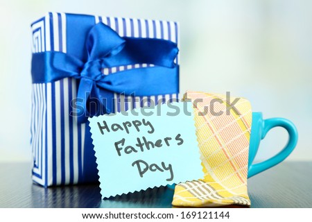 Happy Fathers Day tag with gift boxes, cup and tie, on wooden table, on light background
