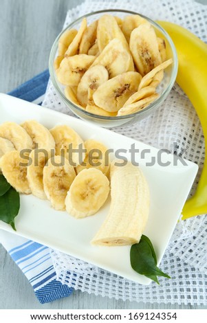Fresh and dried banana slices on plate, on cutting board, on wooden background