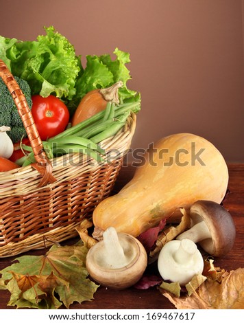 Different vegetables in basket with yellow leaves on table on brown background