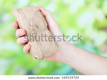 Woman hand holding a telephone wrapped in brown kraft paper, on nature background