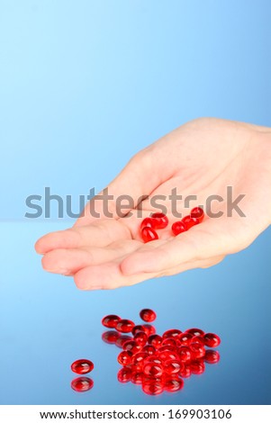 Woman\'s hand holding a red pill on blue background close-up