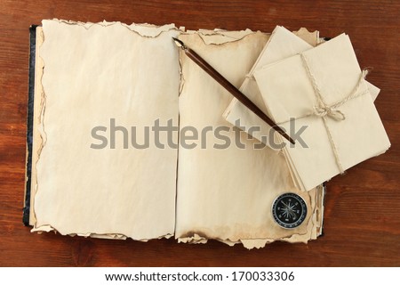 Open old book, letters and compass on wooden background