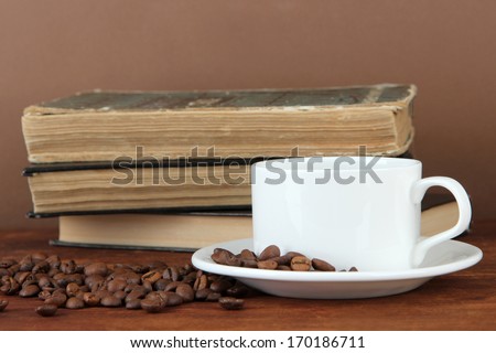 Cup of coffee with coffee beans and books on wooden table on brown background