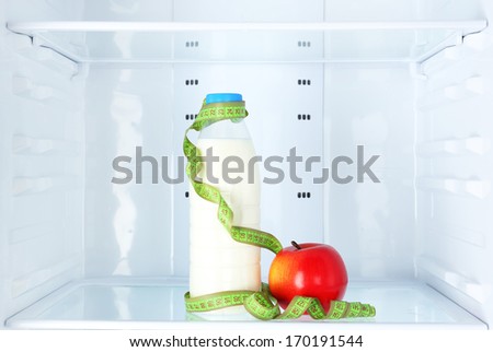 Conceptual photo of diet: apple and milk bottle with measuring type on shelf of refrigerator
