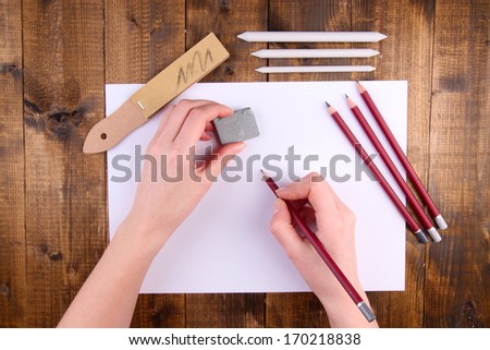 Hands holding pencil and erase with art materials on wooden background