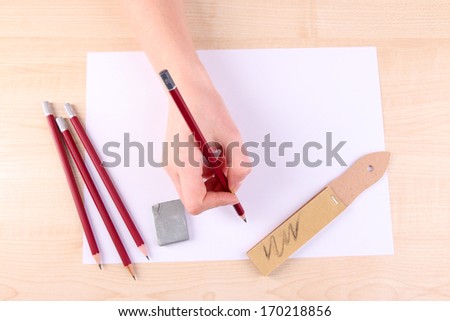 Hand holding pencil with art materials on wooden background