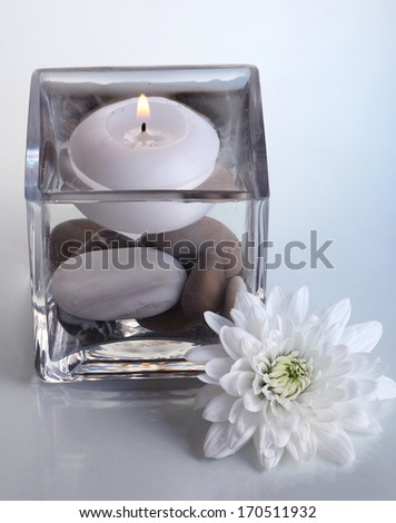 Decorative vase with candle, water and stones on light blue background