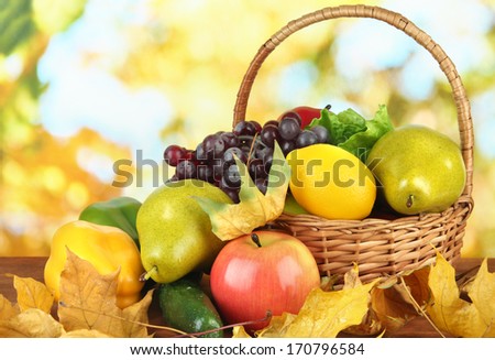 Different fruits and vegetables with yellow leaves in basket on table on bright background