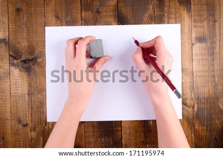 Hands holding pencil and erase with paper on wooden background