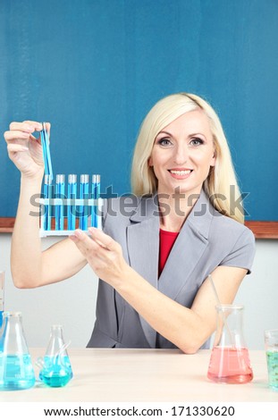 Chemistry teacher with tubes sitting at table on blackboard background