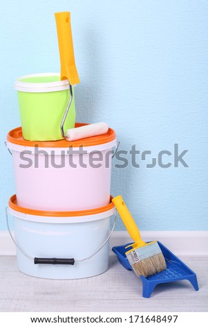 Paints, roll and paintbrush on floor in room on wall background