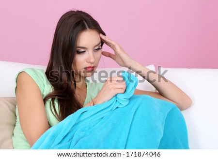 Beautiful young woman sitting on sofa with plaid on pink background