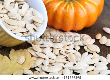 Pumpkin seeds in bowl with pumpkin on table close up