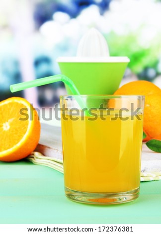 Glass of juice, citrus press and ripe orange on green wooden table