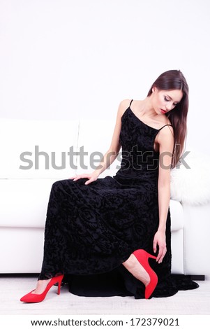 Beautiful young woman in black dress on sofa on white background