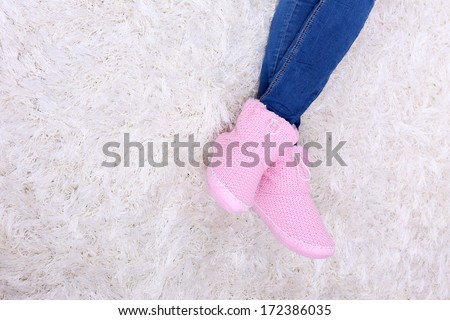 Female legs in blue jeans trousers and home winter shoes, on white carpet background