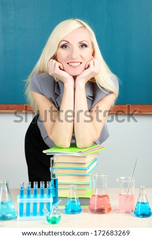Chemistry teacher standing near table with tubes on blackboard background