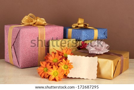Gift boxes with blank label and flowers on table on brown background