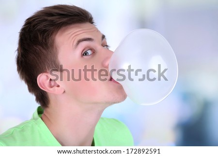 Young man blowing bubble of chewing gum on bright background