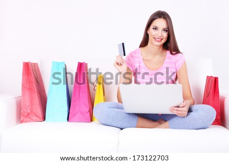 Beautiful young woman holding laptop with shopping bags on sofa on white background