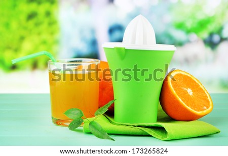 Citrus press, glass of juice and ripe oranges on green wooden table