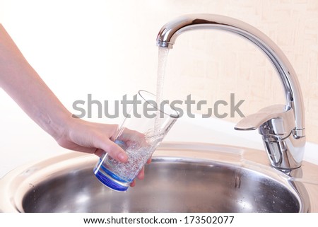 Hand holding  glass of water poured from  kitchen faucet