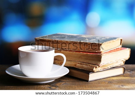 Cup of hot tea with books on table on bright background