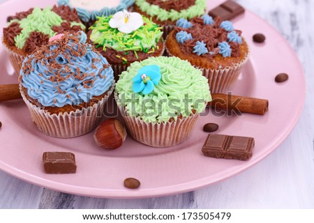 Tasty cupcakes with butter cream, on plate, on color wooden background
