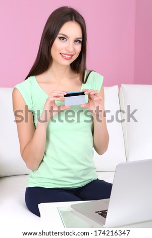 Beautiful young woman sitting on sofa  with laptop on pink background