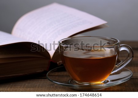 Cup of hot tea with book on table on gray background