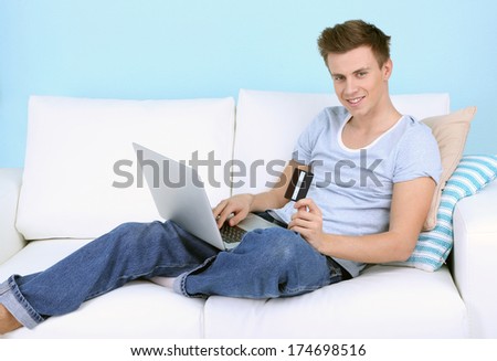 Guy lie on sofa with laptop on blue background