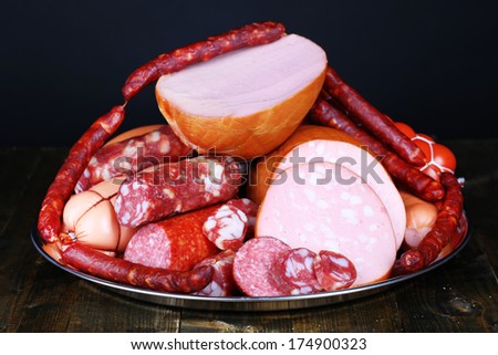 Lot of different sausages on salver on wooden table on black background