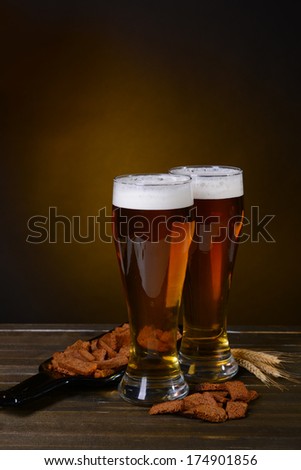 Glasses of beer with snack on table on dark background