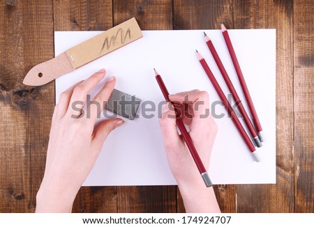 Hands holding pencil with art materials on wooden background