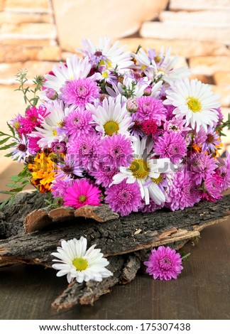 Wildflowers and tree bark on wooden table on stones background