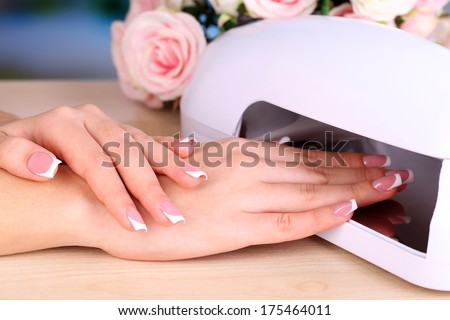 Beautiful woman hands and lamp for nails on table close up