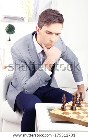 Elegant young businessman sitting on sofa and playing chess, at home