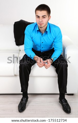 Handsome young man sitting on sofa on light background