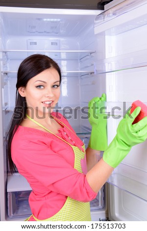 Beautiful young woman washing fridge in kitchen